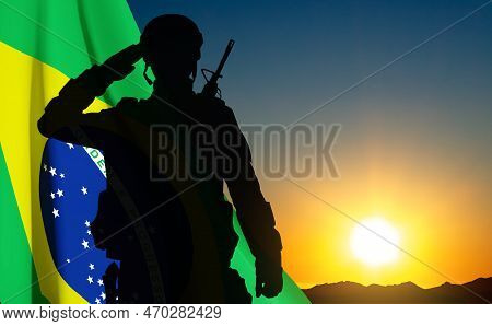 Silhouette Of A Saluting Soldier Against The Sunset With Brazil Flag. Armed Forces Of Brazil Concept