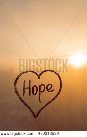 Handwritten Word Hope In Shape Heart On Misted Glass On Window Flooded With Raindrops On Orange Clou
