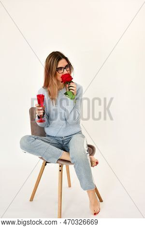 Young Girl Sitting On A Chair Holding A Fresh Red Rose In Her Hand.