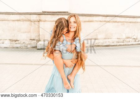 Mother Of The Daughter Walks Playing. Mother Holds The Girl On Her Back, Holding Her Legs, And Her D