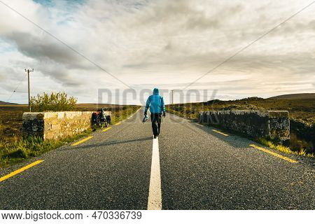 Back View Male Cyclist In Blue Jacket Walk On Road By Touring Bicycle Travel Outdoors In Ireland. Pu