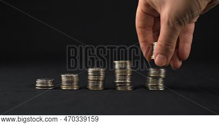 The Hand Reports The Last Stack Of Coins On A Black Background. Five Stacks Of Coins Stand In A Row 