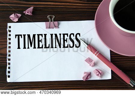 Timeliness - Word On A White Sheet On A Wooden Brown Background With A Cup Of Coffee And A Pen. The 