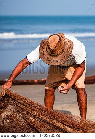 Morjim, North Goa, India , 29 March 2016: Fisherman In A Hat Clean The Fishing Net On The Ocean. Man