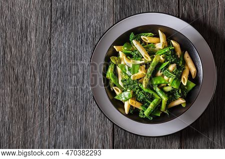 Pasta Primavera With Asparagus, Snap Peas, Broccoli And Kale In Black Bowl On Dark Wood Table, Horiz