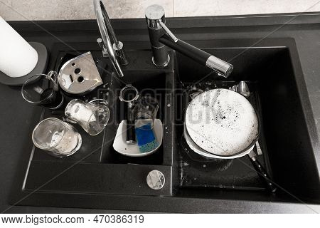 Washing Dishes Concept. Dirty Dishes With Foam From Detergent In A Black Stone Sink In The Kitchen T