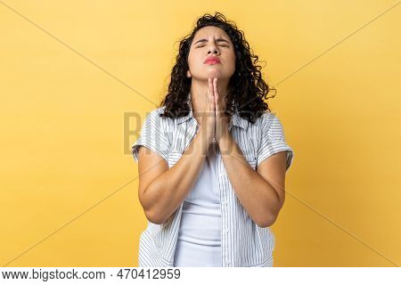 Portrait Of Woman With Dark Wavy Hair Standing Praying Up Heartily, Feeling Guilty, Pleading Begging