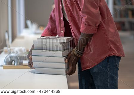 African Student Guy Doing Literature Search In Library, Putting Pile Of Books On Desk, Searching Res