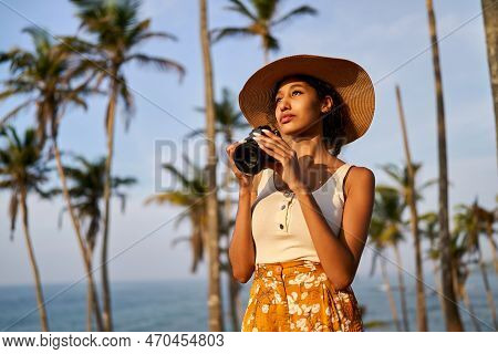 Young African Female Model Tourist With Camera In Colorful Clothes And Straw Hat Taking Pictures At 