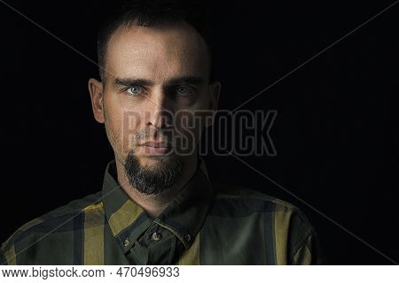 Dramatic Portrait Of A Bearded Man Against A Black Background. Handsome Man In A Checked Shirt In An