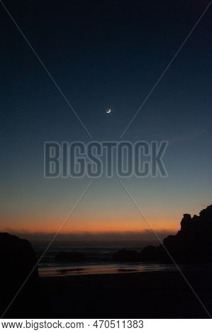 A Cresent Moon Accentuates The Beach During The Golden Hour After Sunset.