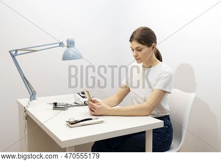 Nail Beautician Hold Gadget, Looking At Smartphone, Sitting At Workstation In Nail Beauty Treatment 