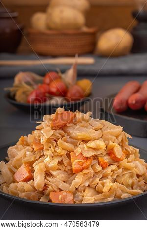 Stewed Cabbage - Bigos In A Black Plate Against The Background Of Pickled Vegetables And Baked Potat