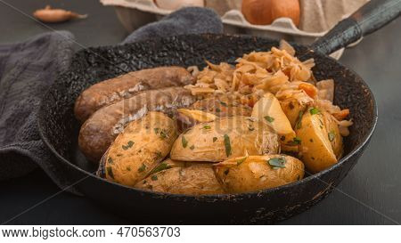 Baked Potato Wedges, Grilled Sausages And Stewed Cabbage Cooked In An Old Cast Iron Skillet. Close-u