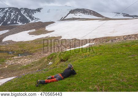 Man Photographing Orange Trollius Flowers On Green Grass With View To Large Snowy Mountain Dome Unde