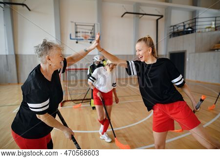 Group Of Young And Old Cheerful Women, Floorball Team Players, In Gym Cebrating Victory.