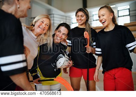 Group Of Young And Old Cheerful Women, Floorball Team Players, In Gym Cebrating Victory.
