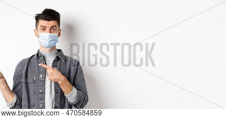 Pandemic Lifestyle, Healthcare And Medicine Concept. Young Guy In Face Mask Inviting Look Here, Poin