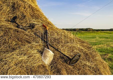 Metal Detector And Sapper Shovel On A Haystack In An Open Field Against The Blue Sky
