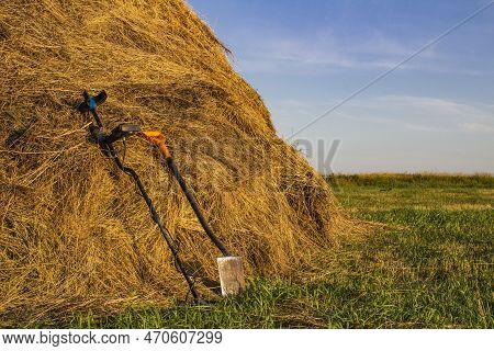 Metal Detector And Sapper Shovel On A Haystack In An Open Field Against The Blue Sky