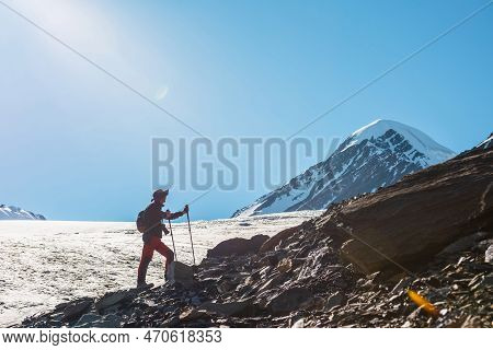 Scenic Alpine Landscape With Silhouette Of Hiker With Trekking Poles Against Large Glacier Tongue An