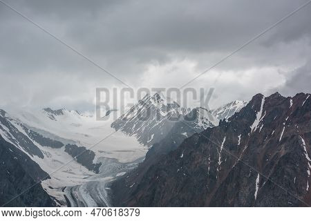 Atmospheric Landscape With Sharp Rocks And High Snowy Mountain Top In Rainy Low Clouds At Overcast. 
