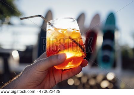 Orange Slice And Aperol Spritz Cocktail On A Stone Against The Backdrop Of A Sandy Beach. Man Holdin