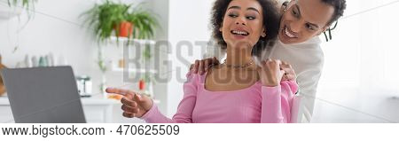 Cheerful African Amercan Freelancer Pointing At Laptop Near Boyfriend At Home, Banner.