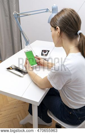 Manicure, Pedicure Professional Holds Smartphone With Green Chroma Key Screen, Sitting At Workstatio