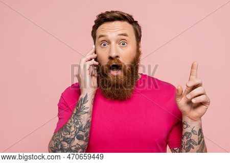 Amazed Tattooed Man Talking On Mobile Phone And Showing Idea Sign Isolated On Pink.