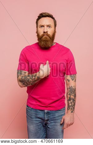 Displeased Bearded Man In Trendy T-shirt Pointing With Finger At Himself Isolated On Pink.