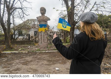 Girl With The Flag Of Ukraine In Her Hands Looks At The Monument Damaged By Shelling. War In Ukraine