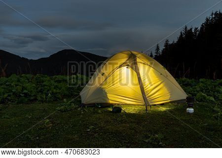 Luminous Tourist Tent In Nature. Tourist Tent And Equipment. Camping. Tent At Dusk. Glowing Tent Aga