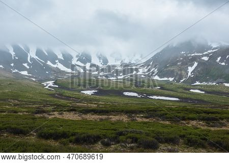 Dramatic Alpine Landscape With Snowy Mountains In Gray Low Clouds. Bleak Atmospheric Scenery Of Tund