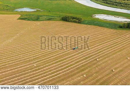 4k Aerial View Tractor Collects Dry Grass In Straw Bales In Wheat Field. Special Agricultural Equipm