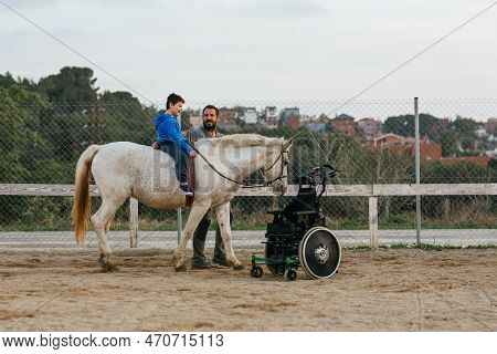 Boy With Disabilities Riding A Horse While Having An Equine Therapy Session With An Instructor.