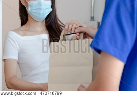 Smiling Young Asian Woman,client Accepting A Delivery Of Bag, Cardboard Box From Delivery Man Wearin