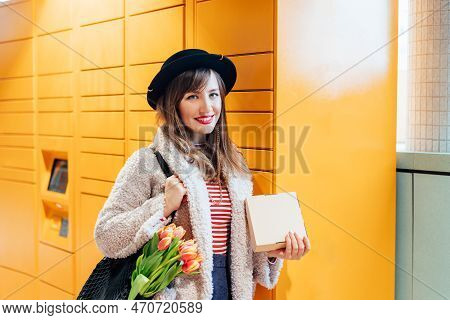Portrait Of Smiling Fashion Woman With Box Near Modern Postal Automatic Mail Terminal With Self Serv