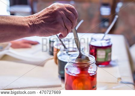 Old Woman Dyeing Easter Eggs At Home In The Kitchen In The Cucumber Glass And With Different Colors,