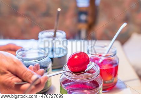 Old Woman Dyeing Easter Eggs At Home In The Kitchen In The Cucumber Glass And With Different Colors,