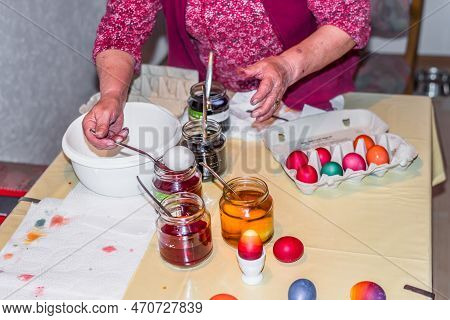 Old Woman Dyeing Easter Eggs At Home In The Kitchen In The Cucumber Glass And With Different Colors,