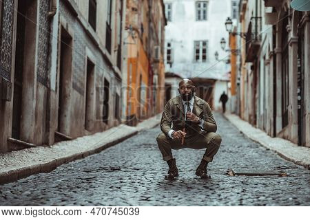 A Shot Focused On A Bald Black Man Dressed In Khaki Overalls Standing In The Middle Of A Black Cobbl