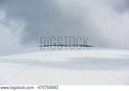 Dramatic Alpine Landscape With Huge Snowy Mountain Dome With Rocky Top In Sunlight Under Gray Cloudy