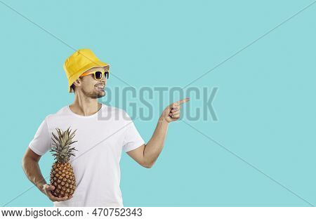 Cheerful Young Caucasian Man In Sunglasses Holding Pineapple And Pointing With Finger At Copy Space