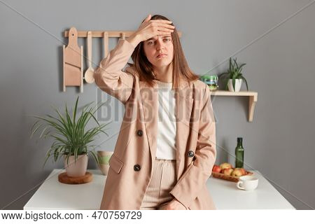 Portrait Of Sad Sick Ill Young Adult Woman Wearing Beige Suit Standing Near Table On Kitchen At Home