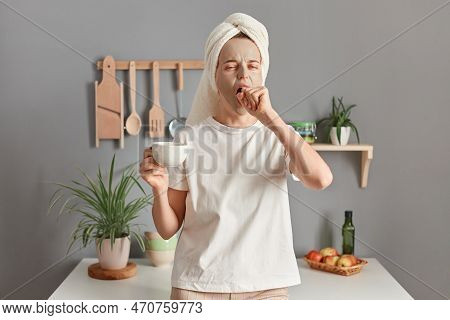 Portrait Of Young Yawning Woman In Towel Wrapped Around Hair, With Morning Cup Of Coffee, Standing I