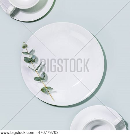 Clean, Empty White Dishes And Cups With Eucalyptus Twig On Blue Background. Eco Friendly Washing Dis