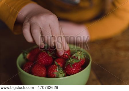 Close-up Of A Child's Hand Picking Strawberries From A Bowl