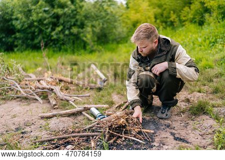 Bearded Survivalist Male In Raincoat Putting Brushwood On Campfire To Making Fire In Forest On Cloud