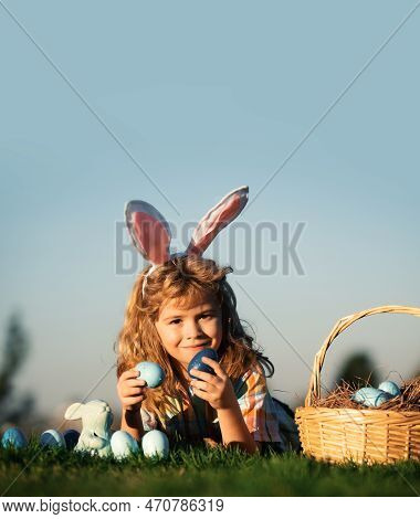 Child With Easter Eggs In Basket Outdoor. Boy Laying On Grass In Park, On Sky Background With Copy S